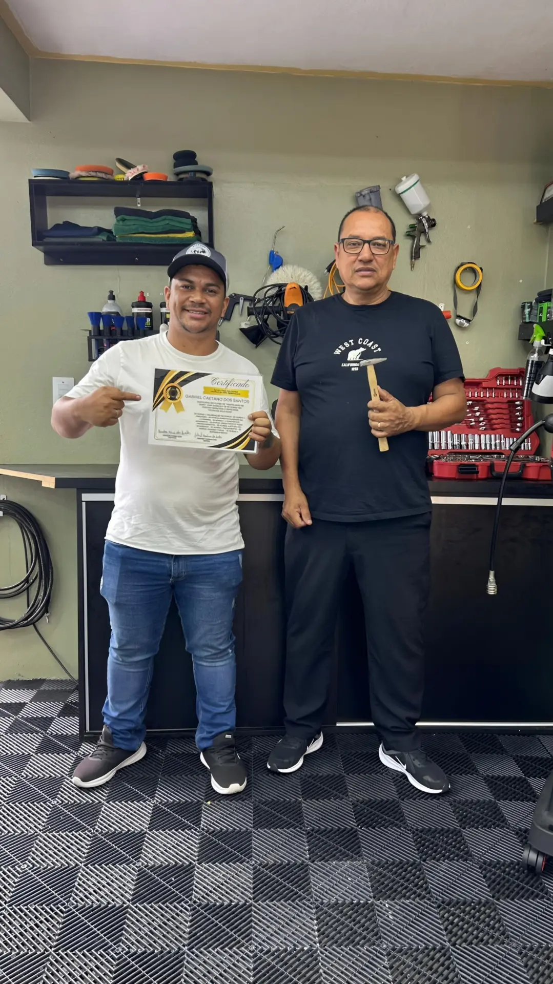Aluno recebendo certificado ao lado do instrutor Sandro na oficina